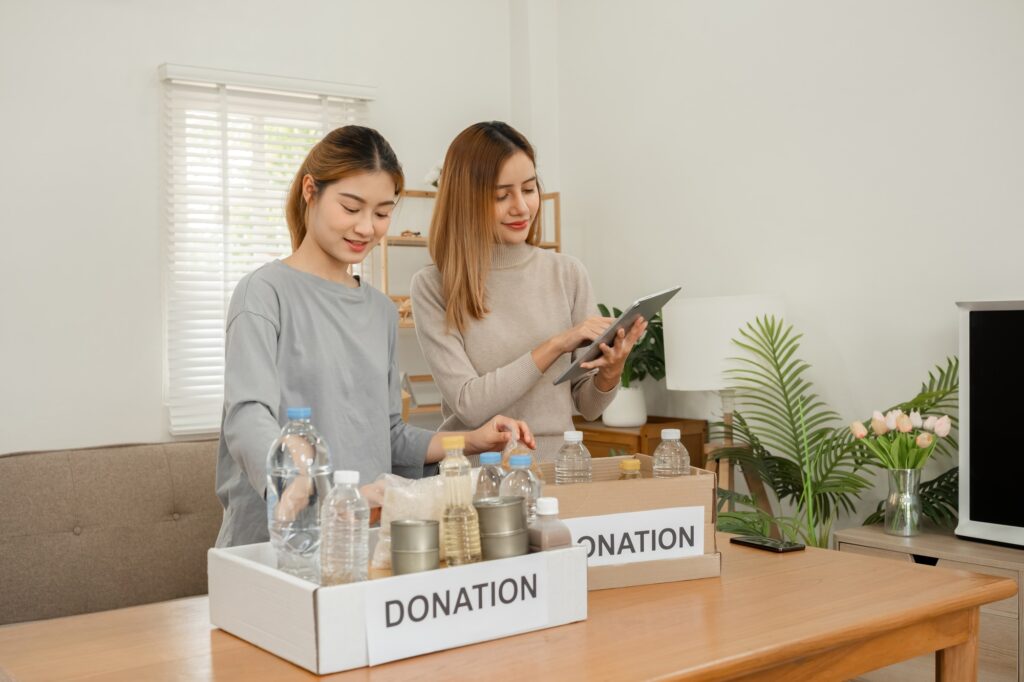 Two young female volunteers help pack food into donation boxes and prepare donation boxes to take to
